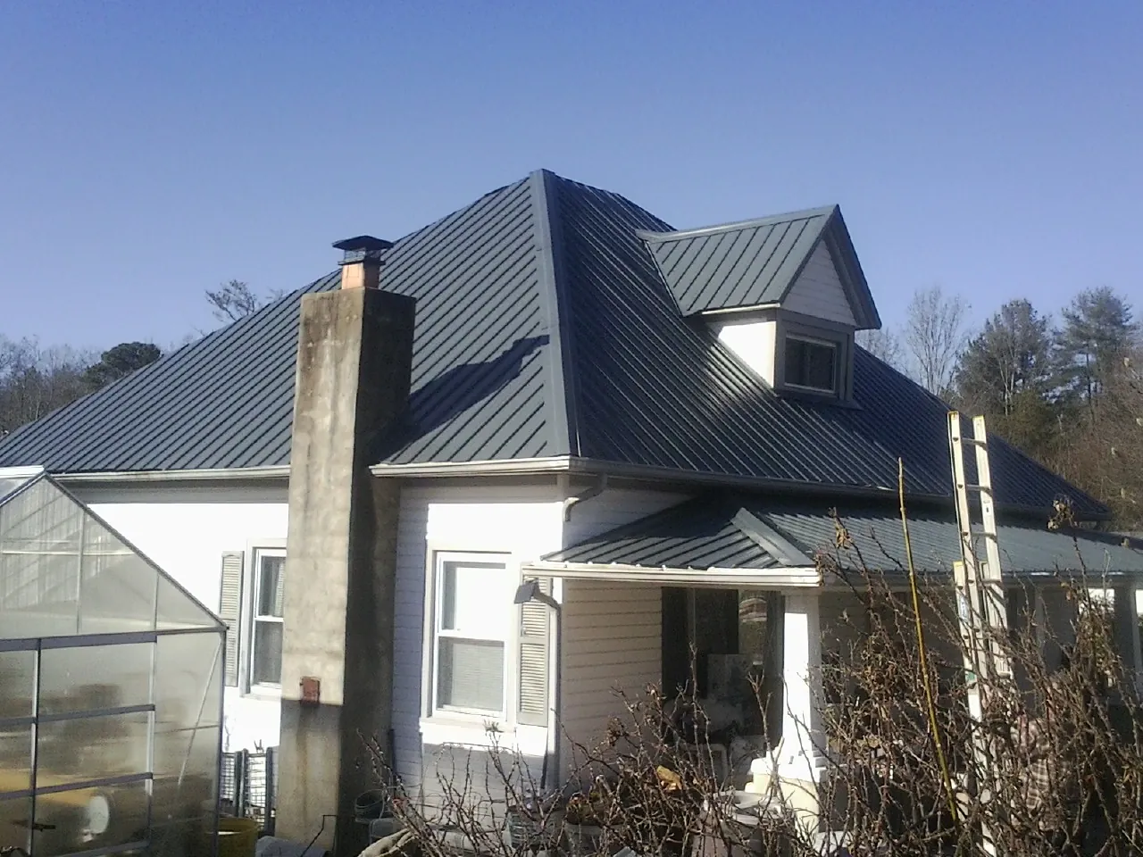 Dark blue standing seam metal roof on a white farmhouse with dormer — Slate & Tile Roof Repair by Roofing Brothers in Tannersville