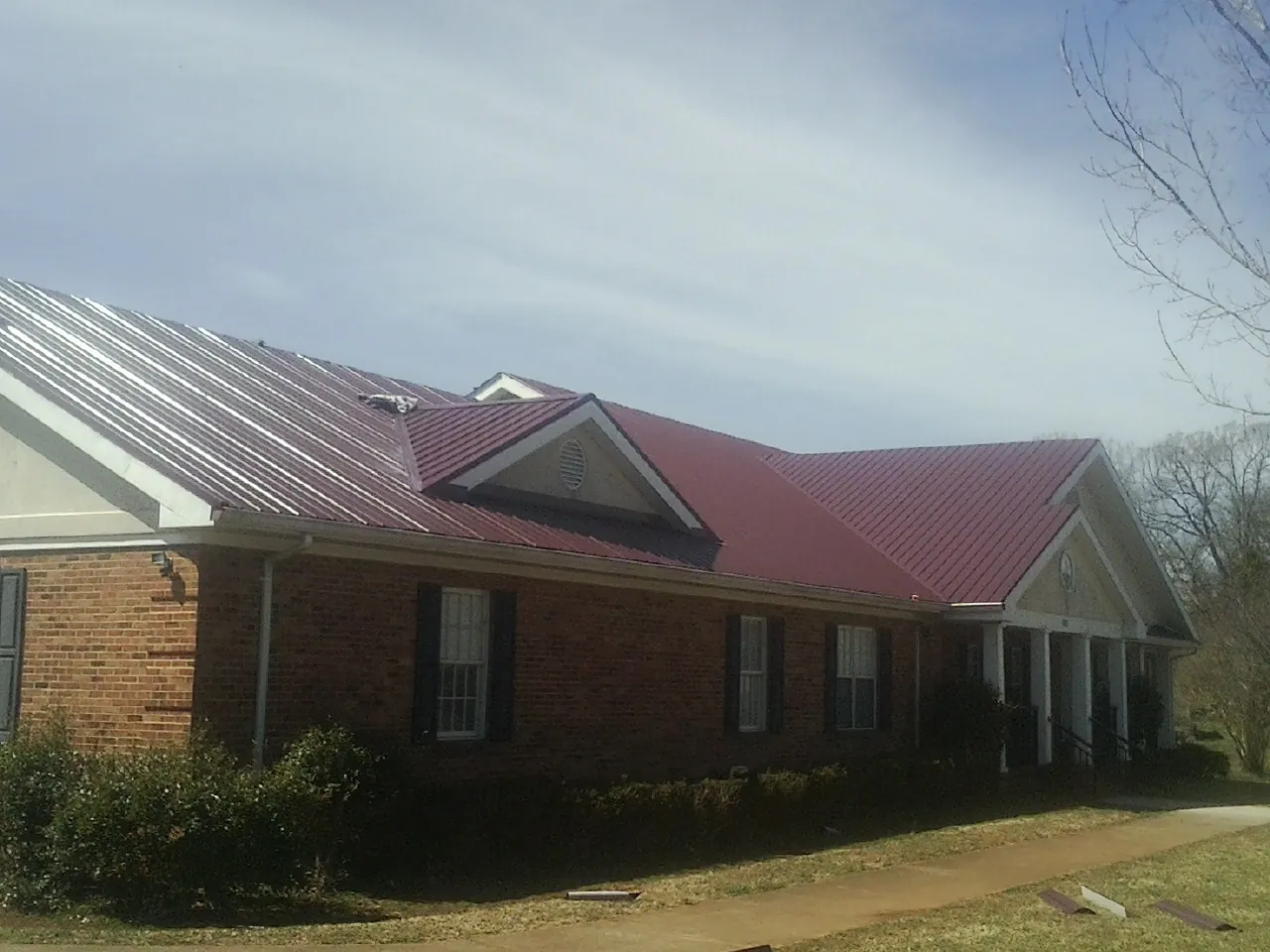 Red metal roof with gabled entries on a long brick building, from a Hail Damage Roof Repair job in Tannersville