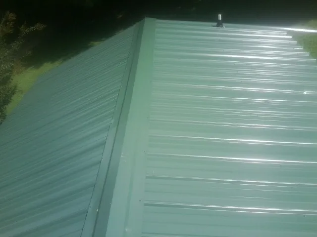 New green metal panels meeting at the ridge of a roof — Flat Roof Repair work by our crew in Tannersville
