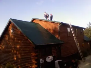 Crew on the ridge of a green metal roof on a two story log home in Tannersville