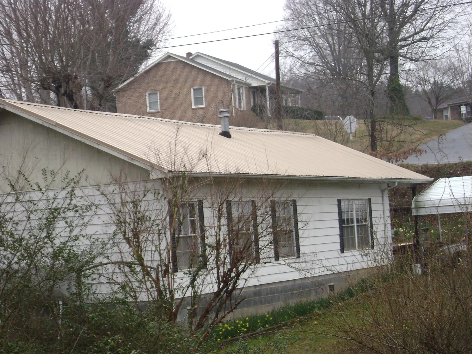 Tan metal roof on a white sided house set into a hillside — Commercial Roofing by Roofing Brothers in Tannersville